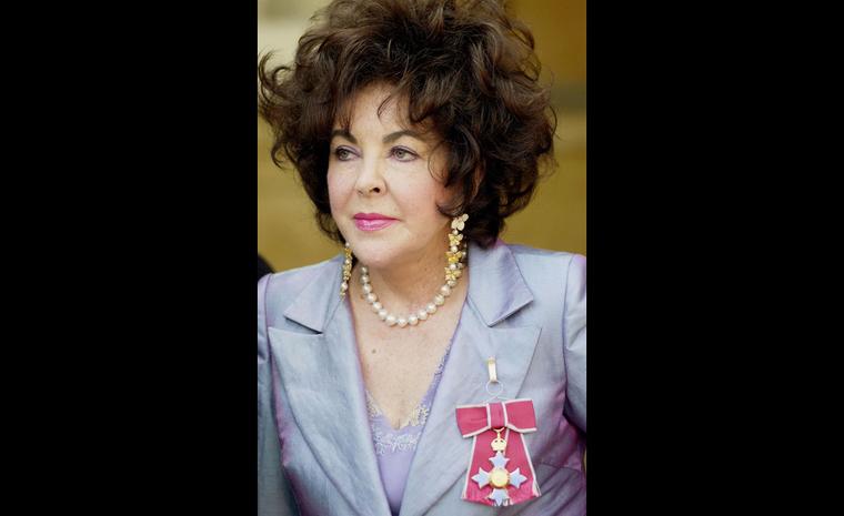 In 2000 receiving her Dame Commander of the Order of the British Empire wearing coral, diamond and yellow sapphire earrings by Van Cleef & Arpels.