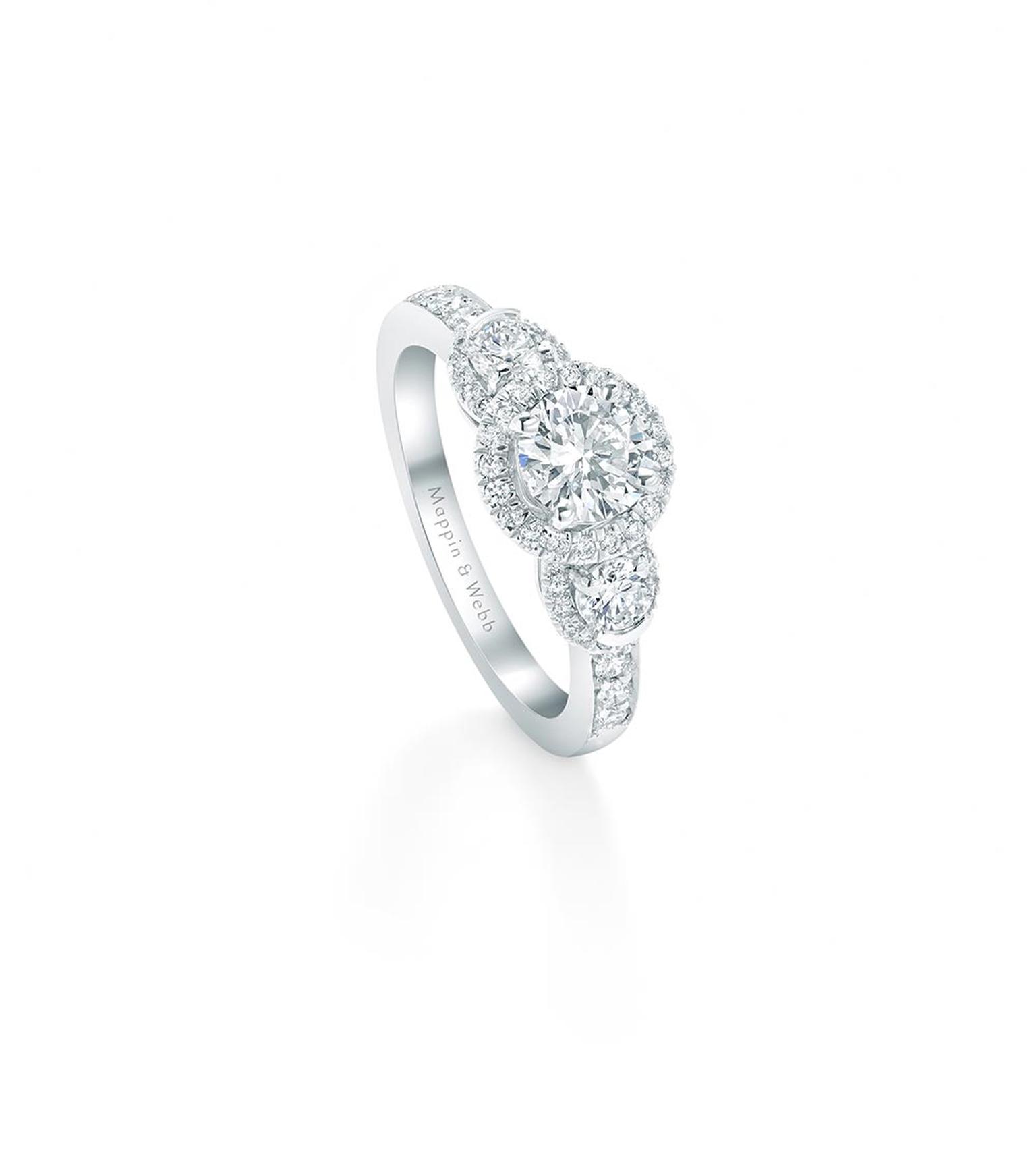 Mappin & Webb Eglantine engagement ring featuring a trio of diamonds encircled by a sparkling halo setting with ?a cushion-cut solitaire at its centre