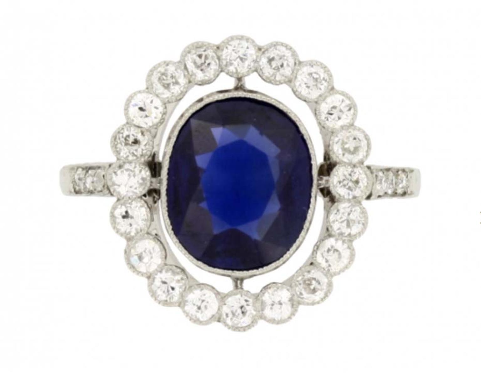This Edwardian marquise sapphire and diamond cluster engagement ring circa 1910, available at Berganza, is set with a marquise shape, old-cut, natural unenhanced sapphire, encircled by a single row of round, old, single-cut diamonds of varying sizes, with