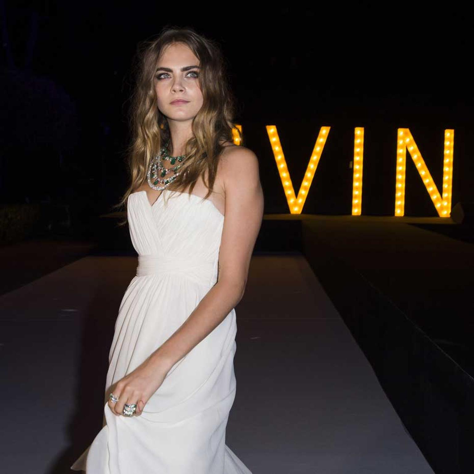 Arriving at de GRISOGONO's "Divine in Cannes" party, Cara Delevingne cuts a striking figure in an angelic white dress accessorised with a unique emerald, diamond and ruby high jewellery necklace.