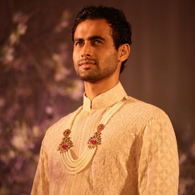 A model sporting a nehru jacket with a multi-string pearl necklace featuring kundan polki and gem-set brooches by Anmol Jewellers.