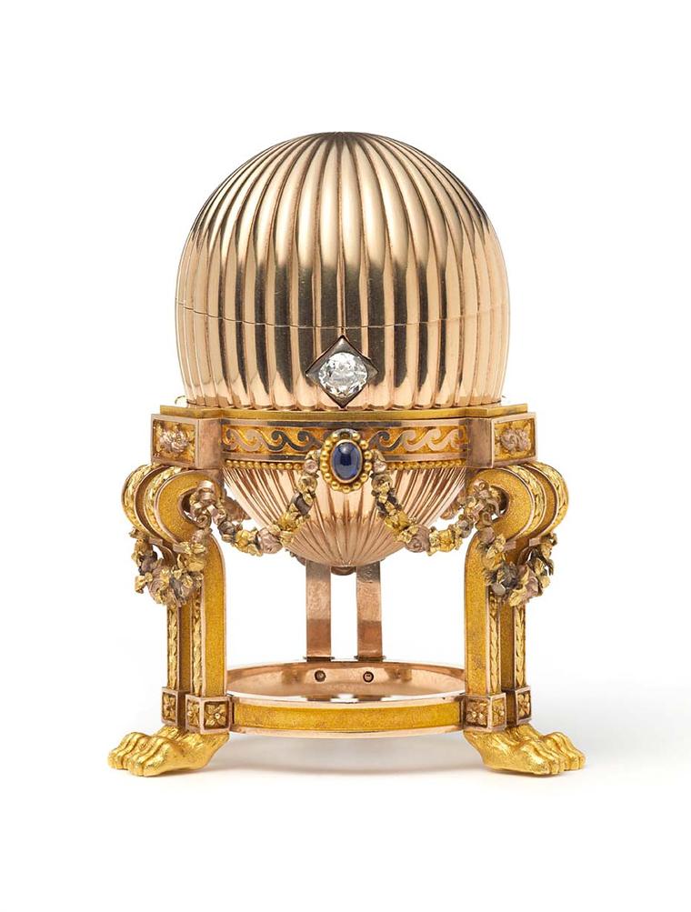 The yellow gold Imperial Faberge Easter Egg contains a Vacheron Constantin watch with diamond set gold hands. The egg sits on a stand with lions paw feet, decorated with gold garlands and three cabochon blue sapphires topped with rose diamond set bows.