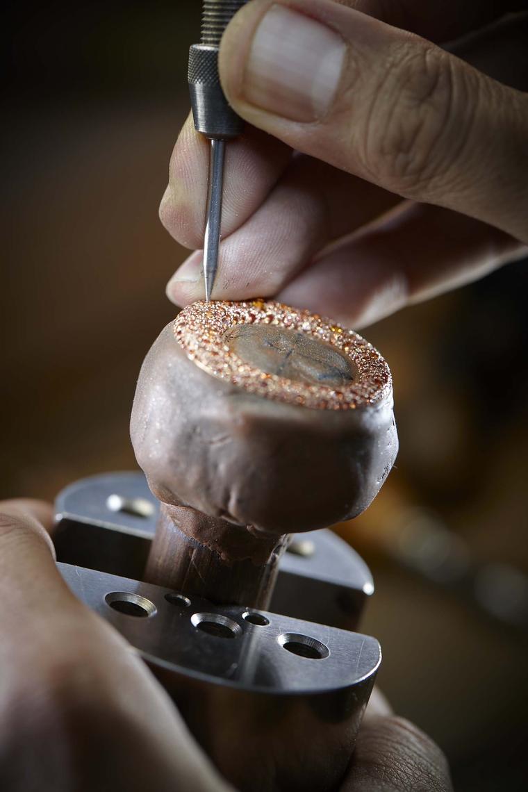 The orange sapphires on the inner bezel are set using the painstaking technique of snow setting. A series of different-sized wells are bored into the pink gold by hand and then set with orange sapphires in varying shades and sizes to cast a mantle of oran