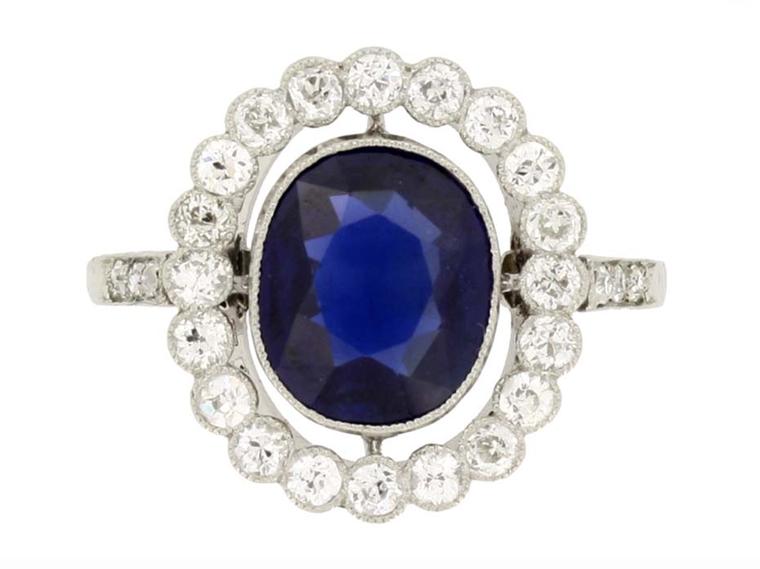 This Edwardian marquise sapphire and diamond cluster engagement ring circa 1910, available at Berganza, is set with a marquise shape, old-cut, natural unenhanced sapphire, encircled by a single row of round, old, single-cut diamonds of varying sizes, with