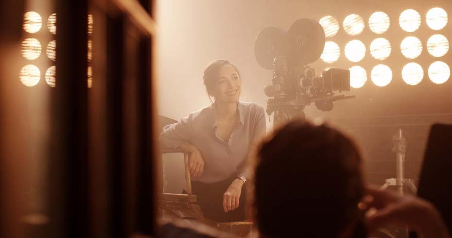 Carmen Chaplin is captivated by a silent movie, possibly starring her grandfather Charlie Chaplin, surrounded by film equipment of his era and lit by the hazy light of studio spotlights during the shoot for Jaeger-LeCoultre's new Open a Whole New World ad